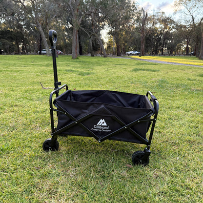 Black folding camping wagon on grass with trees in the background