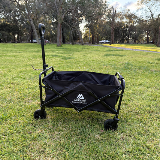 Black folding camping wagon on grass with trees in the background
